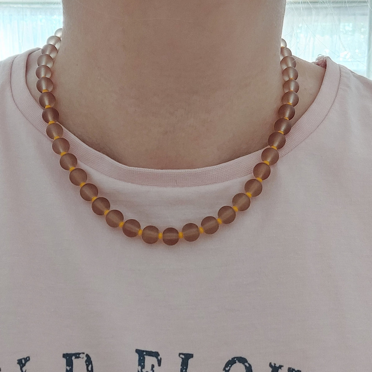 A close-up of a person wearing a beaded necklace made of frosted brown beads separated by tiny orange beads