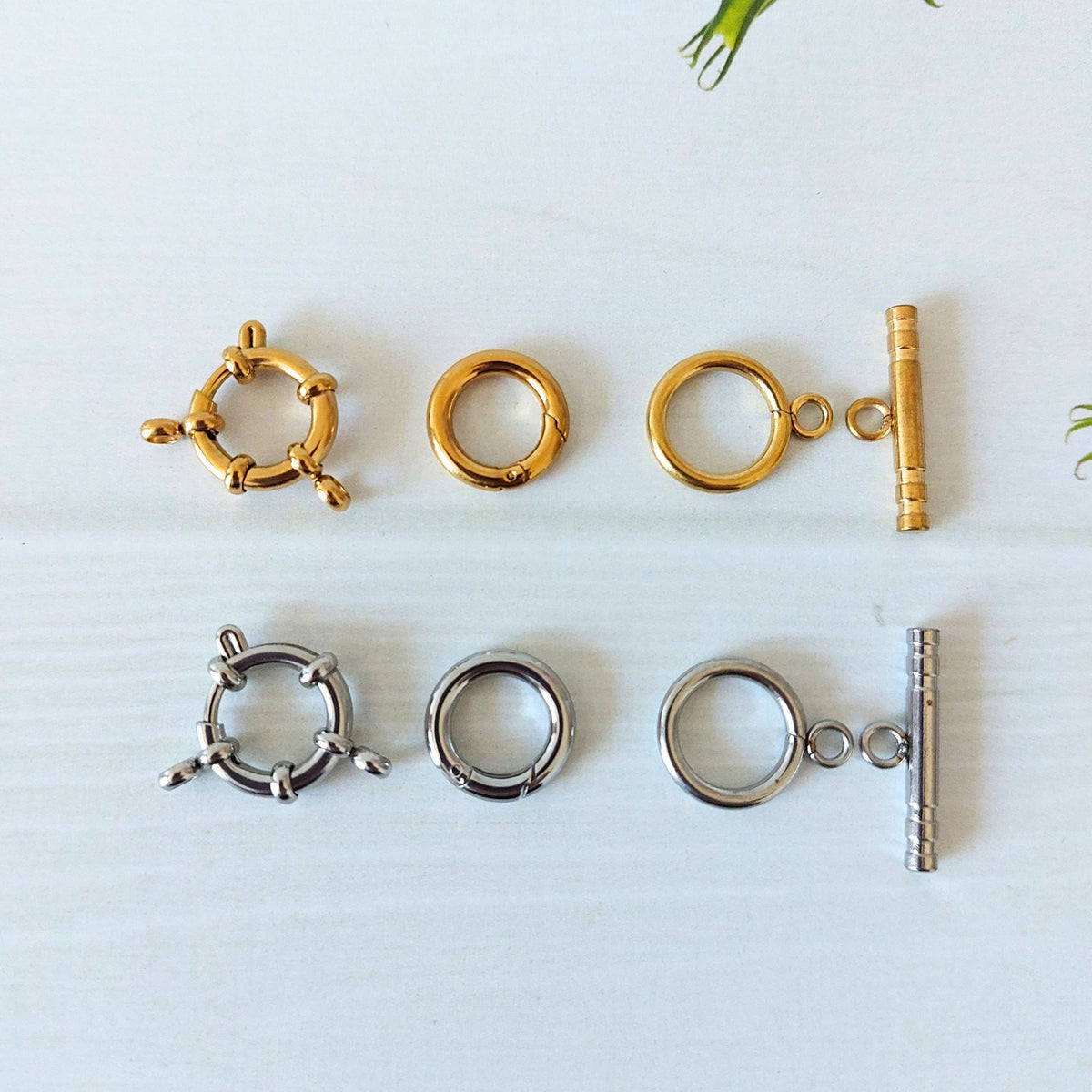 Six small jewellery findings arranged on a white surface: three gold-plated and three silver-tone clasp components, each metal available in a bolt ring clasp, hinged circle clasp and a circle toggle clasp with a bar.
