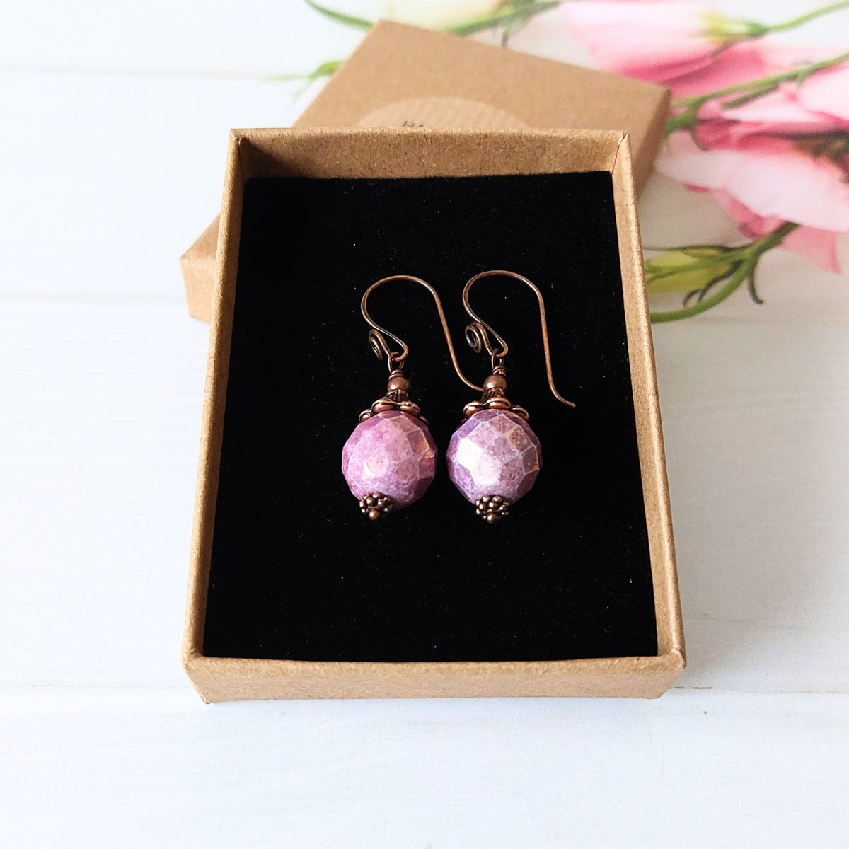 A pair of handmade dangle earrings with faceted lavender beads and copper fishhook wires, presented in an open brown kraft gift box.