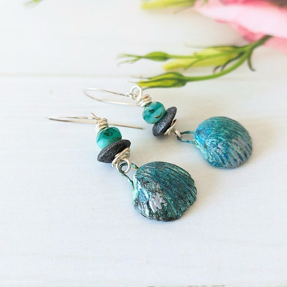 Aqua-blue faceted glass beads with grey disc beads wire-wrapped to hand-painted polymer clay shell drops on silver-plated earwires. Shown on wooden backdrop.
