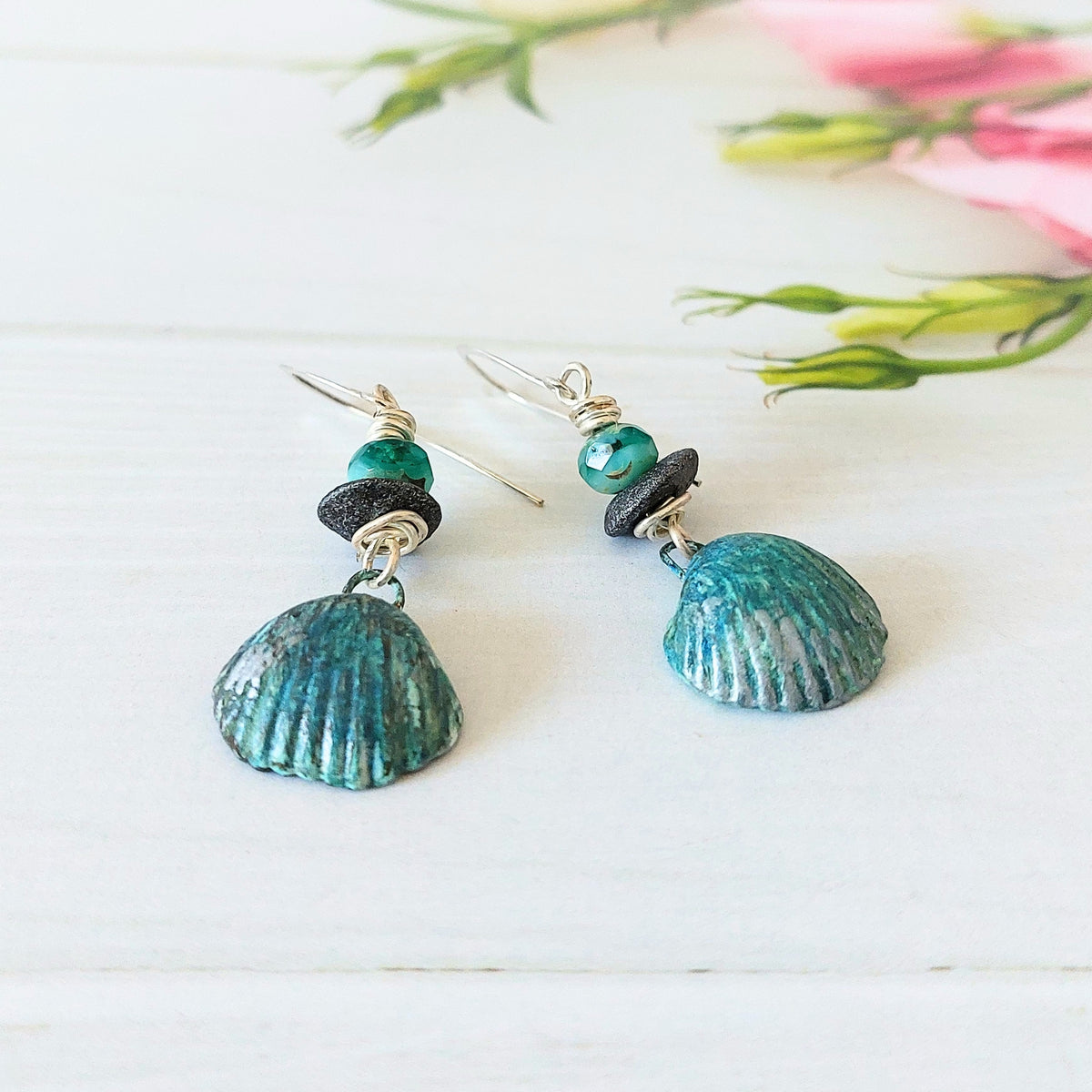 Aqua-blue faceted glass beads with grey disc beads wire-wrapped to hand-painted polymer clay shell drops on silver-plated earwires. Shown on wooden backdrop.